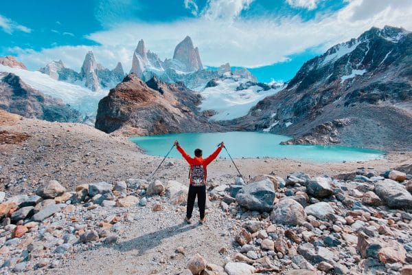 Argentina: De la Selva al Glaciar, un Viaje de Extremos Hombre con equipo de esquí o senderismo de invierno alzando los brazos frente a un lago de montaña en los Andes argentinos.