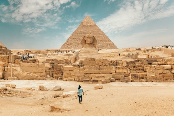 Egipto: Un Viaje Eterno por el Corazón del Nilo Una persona de espaldas contemplando la Esfinge y una pirámide, símbolos de un viaje por el corazón del Nilo en Egipto.