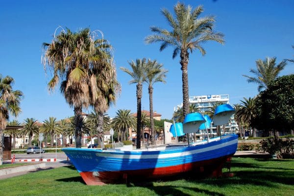 Guía de Salou y la Costa Dorada: Playas, Aventura y Gastronomía Una barca de pescadores de color azul en un jardín rodeado de palmeras que ilustran a Salou