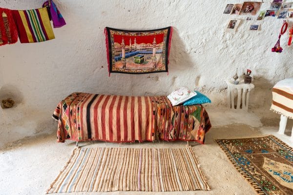Guía para Viajar a Túnez: Ruta Esencial de 7 Días Interior de una habitación blanca con alfombras y cama en el suelo cubierta por mantas de colores que ilustran a Túnez