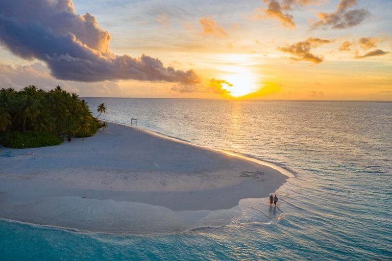 Playa de arena blanca con ocaso de sol al fondo que ilustran a Tahití y sus islas
