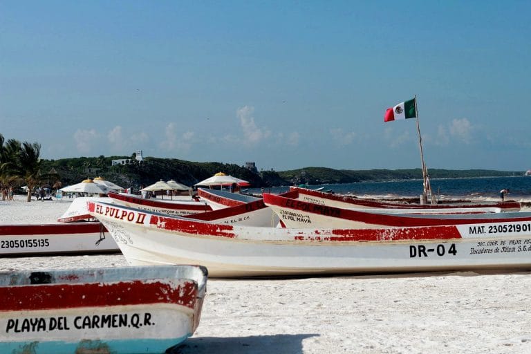 Botes de pescadores sobre una playa con la bandera de Méjico que ilustra la costa de la riviera Maya