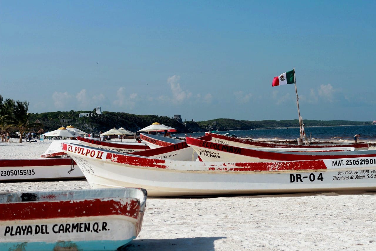 Botes de pescadores sobre una playa con la bandera de Méjico que ilustra la costa de la riviera Maya