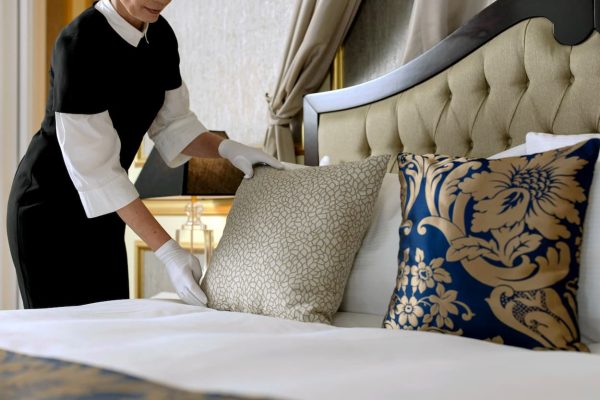 Mucama con guantes blancos arreglando cojines en cama de suite de crucero de lujo