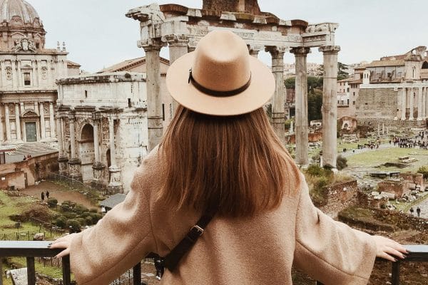 Una chica elegante con sombrero frente a ruinas romanas, representando una experiencia cultural única en Roma lejos de las multitudes.
