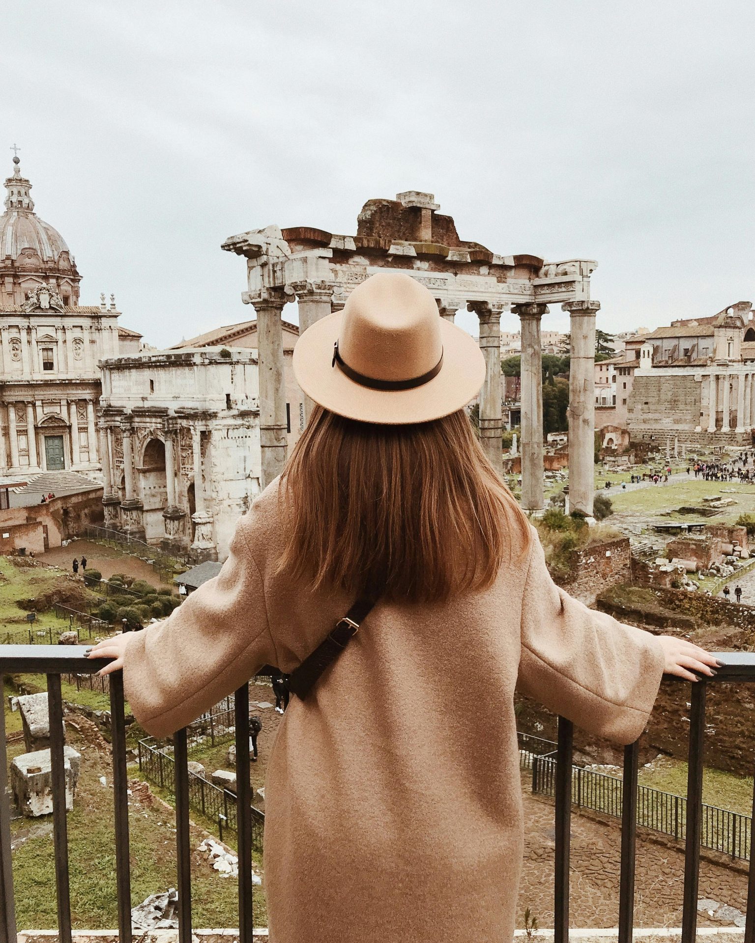 Una chica elegante con sombrero frente a ruinas romanas, representando una experiencia cultural única en Roma lejos de las multitudes.