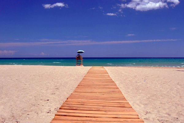 Un sendero de madera sobre la playa que conduce al mar, representando un viaje en familia o grupo para alquilar una villa.