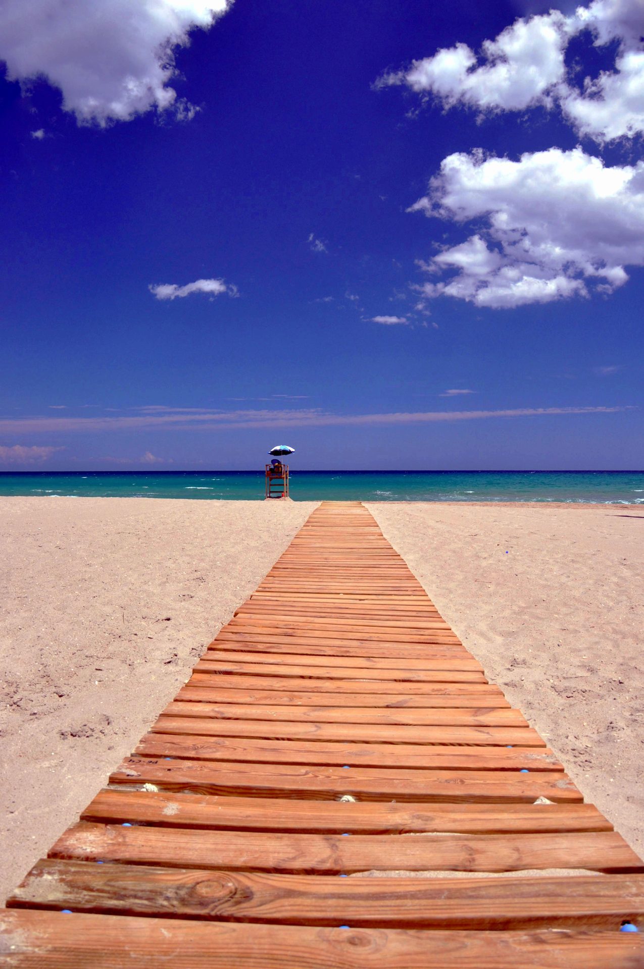 Un sendero de madera sobre la playa que conduce al mar, representando un viaje en familia o grupo para alquilar una villa.