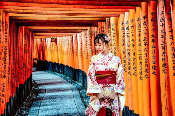Kyoto a Puerta Cerrada: Un Viaje al Corazón de la Tradición Una mujer en kimono caminando por un pasillo con elementos de escritura japonesa, representando un viaje al corazón de la tradición en Kioto.