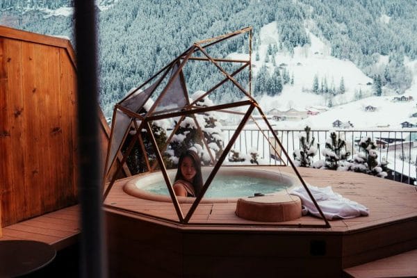 Esquí en los Alpes Suizos: Lo Que No Muestran las Fotos una chica dentro de un jacuzzi en la terraza de un hotel con el fondo de una montaña nevada