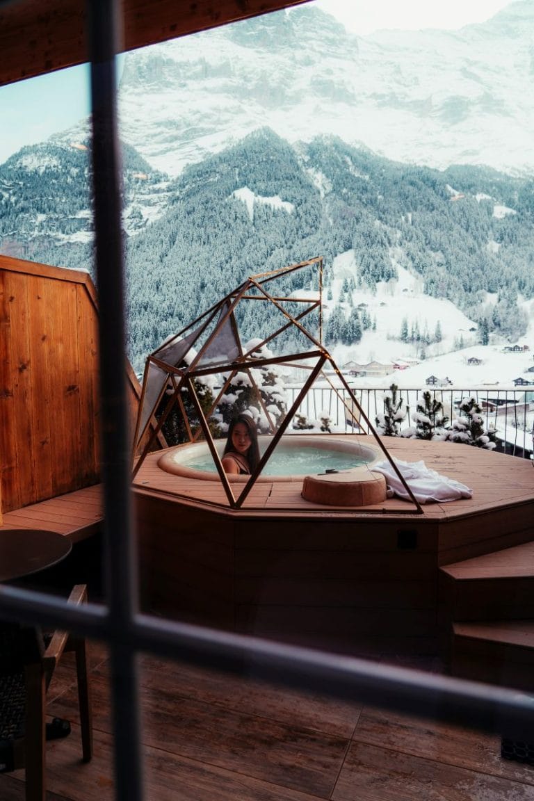 una chica dentro de un jacuzzi en la terraza de un hotel con el fondo de una montaña nevada