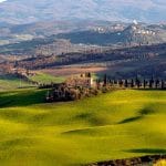 El Encanto Oculto de la Toscana: Un Viaje por la Cultura y la Gastronomía Panorámica de colinas llenas de viñas y en el medio de la imagen una casona tipica de la Toscana