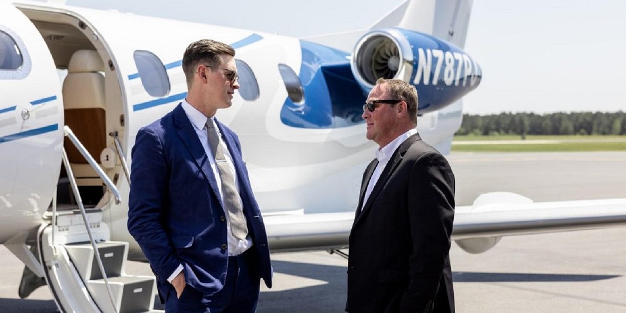 Viajero de lujo con chaqueta azul y gafas conversando con personal en la escalera de un jet privado, simbolizando una logística de viaje sin fisuras.