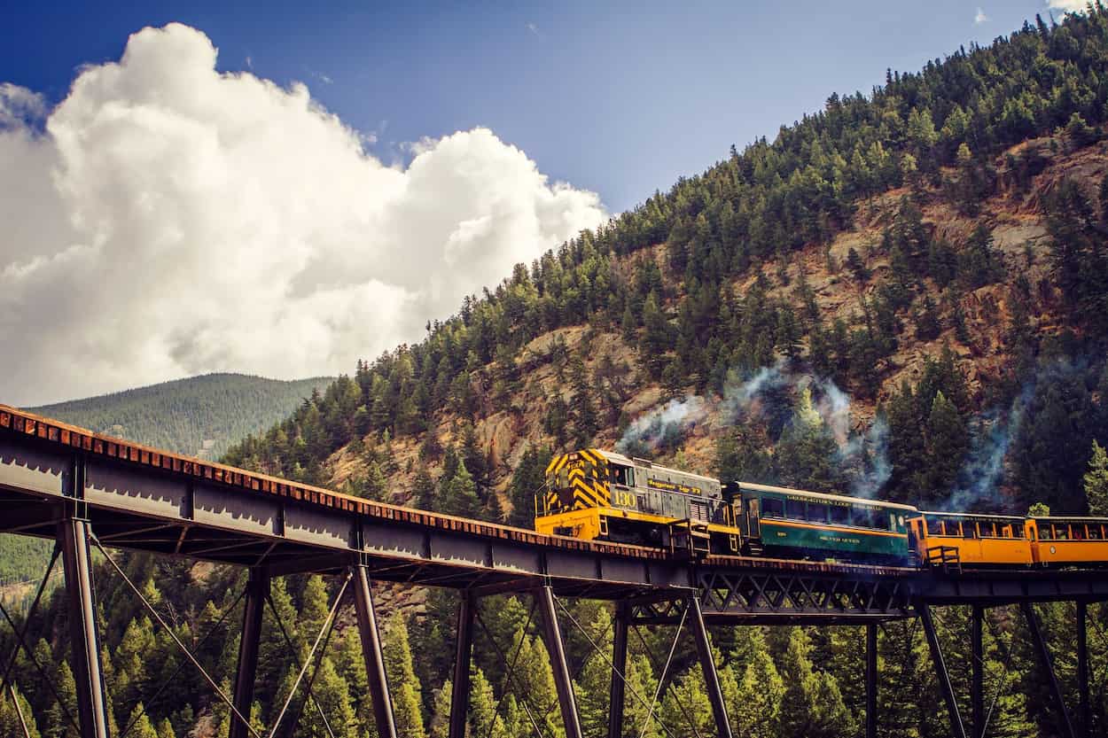 Tren amarillo de lujo cruzando gigantesco acueducto de hierro entre colinas