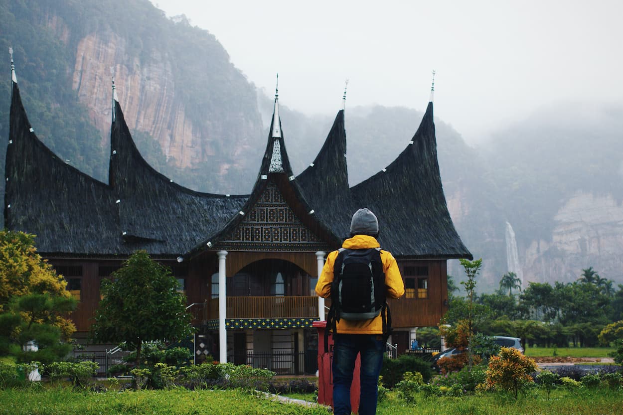 Viajero con mochila contemplando templo en montañas neblinosas en viaje de lujo en solitario