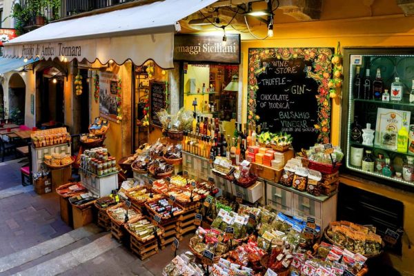 Tienda de alimentos con productos típicos de Sicilia expuestos en la calle de Taormina al atardecer.