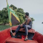 Proa bote con bandera Jamaica sostenida pie hombre dirigiéndose islote caribeño