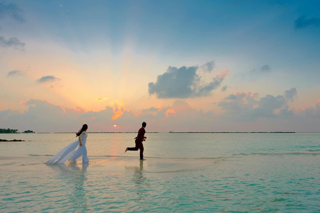 Pareja vestida de novios corriendo en una playa al borde del agua durante el atardecer en Isla Mauricio