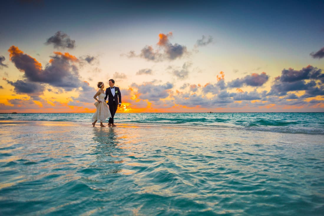 Pareja vestida de novios corriendo en una playa al borde del agua durante el atardecer en Isla Mauricio