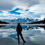 Silueta de mujer de espaldas mirando hacia una montaña nevada al borde de un lago helado en la Patagonia Argentina