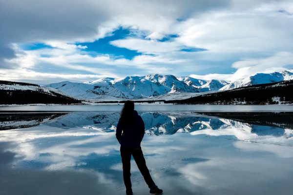 Silueta de mujer de espaldas mirando hacia una montaña nevada al borde de un lago helado en la Patagonia Argentina