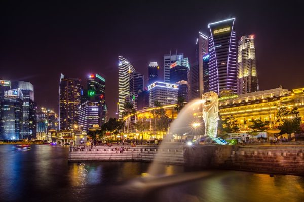 Merlion de Singapur con chorro de agua iluminado y el skyline nocturno de Marina Bay al fondo visto desde el mar