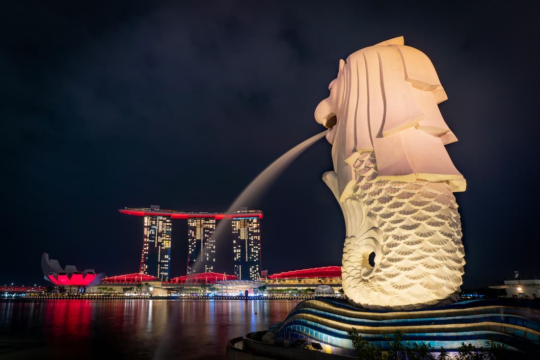 Merlion y skyline nocturno de Marina Bay — el icono más reconocible de Singapur Merlion de Singapur con chorro de agua iluminado y el skyline nocturno de Marina Bay al fondo visto desde el mar