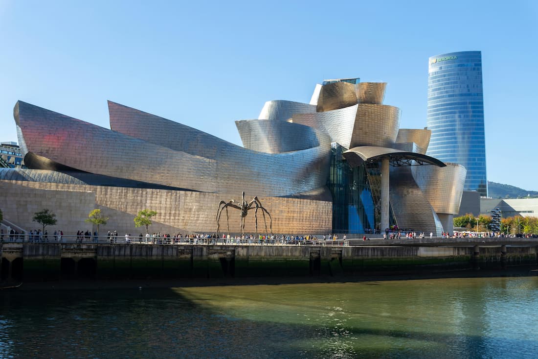 Museo Guggenheim Bilbao — fachada de titanio junto al río Nervión Fachada exterior del Museo Guggenheim Bilbao con su estructura de titanio reflejada en el río Nervión