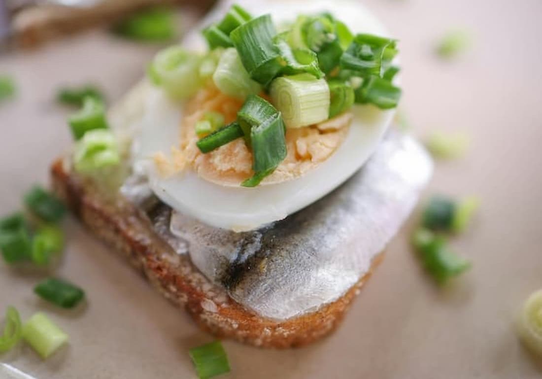 Plato de smørrebrød danés con pan de centeno oscuro, arenque marinado y guarnición en restaurante de Copenhague