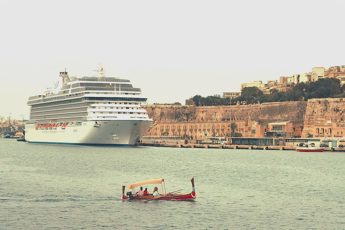 Vista aérea de un gran crucero atracado en un puerto histórico mediterráneo con ciudad al fondo