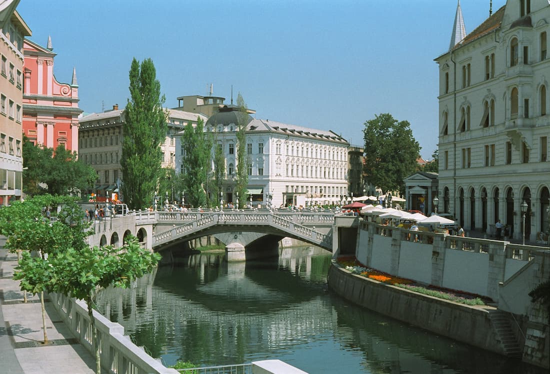 Terrazas de bares junto al río Ljubljanica al atardecer con el Puente Triple de Plečnik al fondo en Liubliana