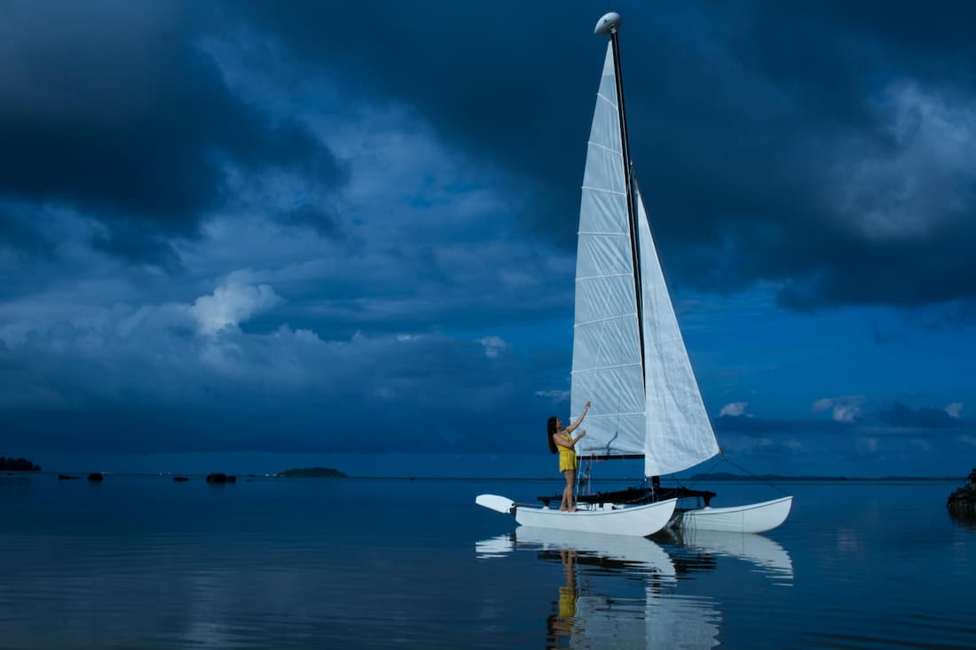 Catamarán en la laguna de Bora Bora — navegación en aguas azul espejo en Tahití Chica izando las velas de un pequeño catamarán en la laguna de aguas azul espejo de Bora Bora en Tahití