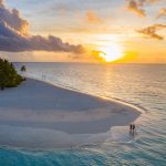 Pareja caminando por una playa de arena blanca al atardecer en Tahití vista desde el aire