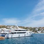 Cinco yates de lujo amarrados en un muelle en una bahía mediterránea con casas blancas sobre la colina al fondo
