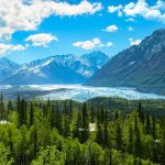 Vista panorámica de un gran lago de Alaska rodeado de bosques y montañas nevadas reflejadas en el agua