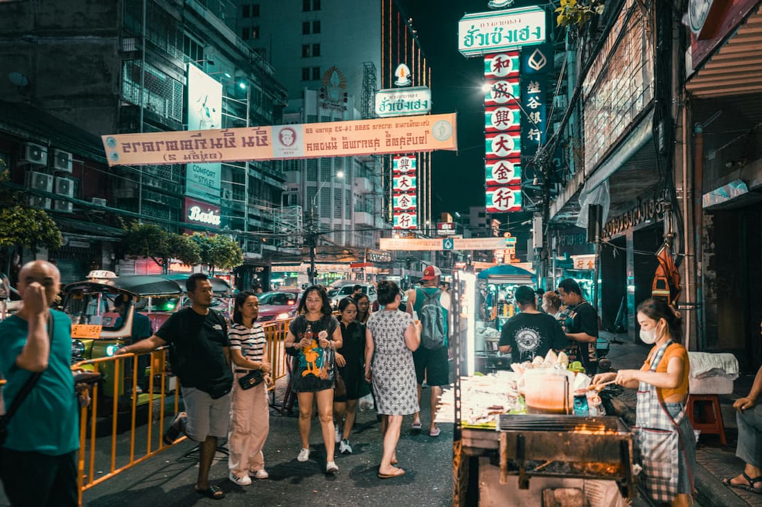 Calle de Chinatown en Bangkok de noche con letreros de neón dorado y puestos de comida callejera en Yaowarat
