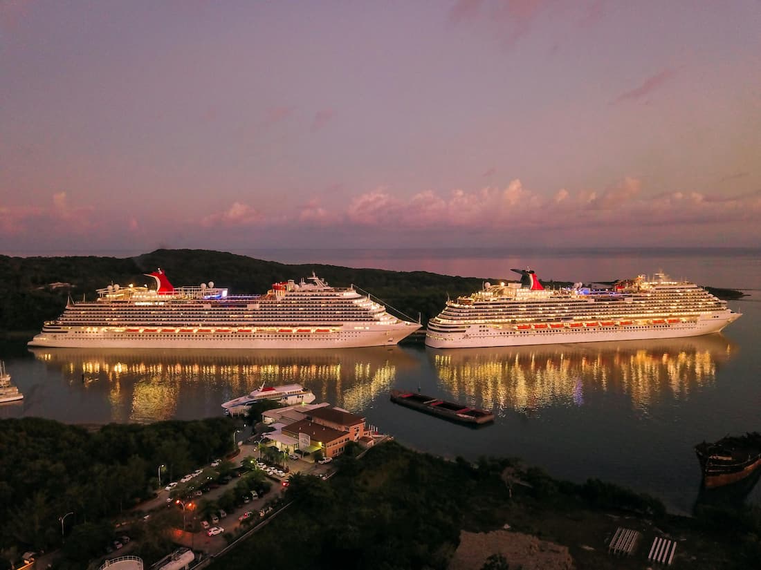 Dos cruceros de lujo amarrados en puerto de noche con luces reflejadas en el agua