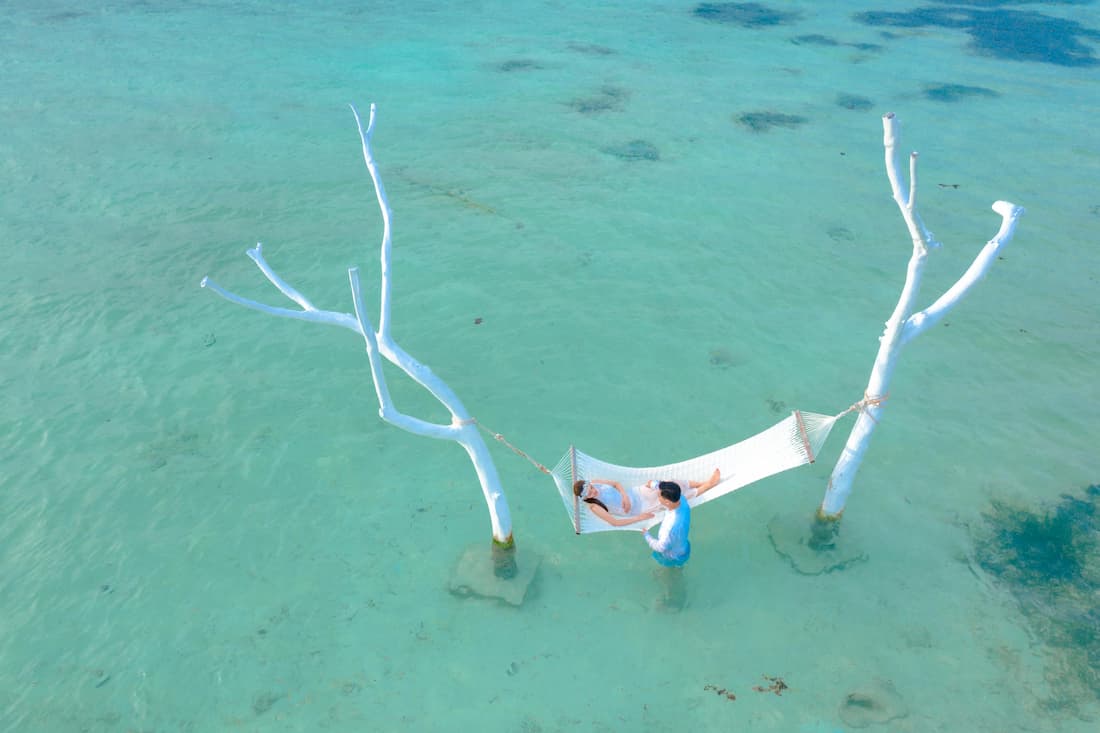 Pareja disfrutando de hamaca sobre agua cristalina en playa privada del Caribe estilo Isla Necker Richard Branson