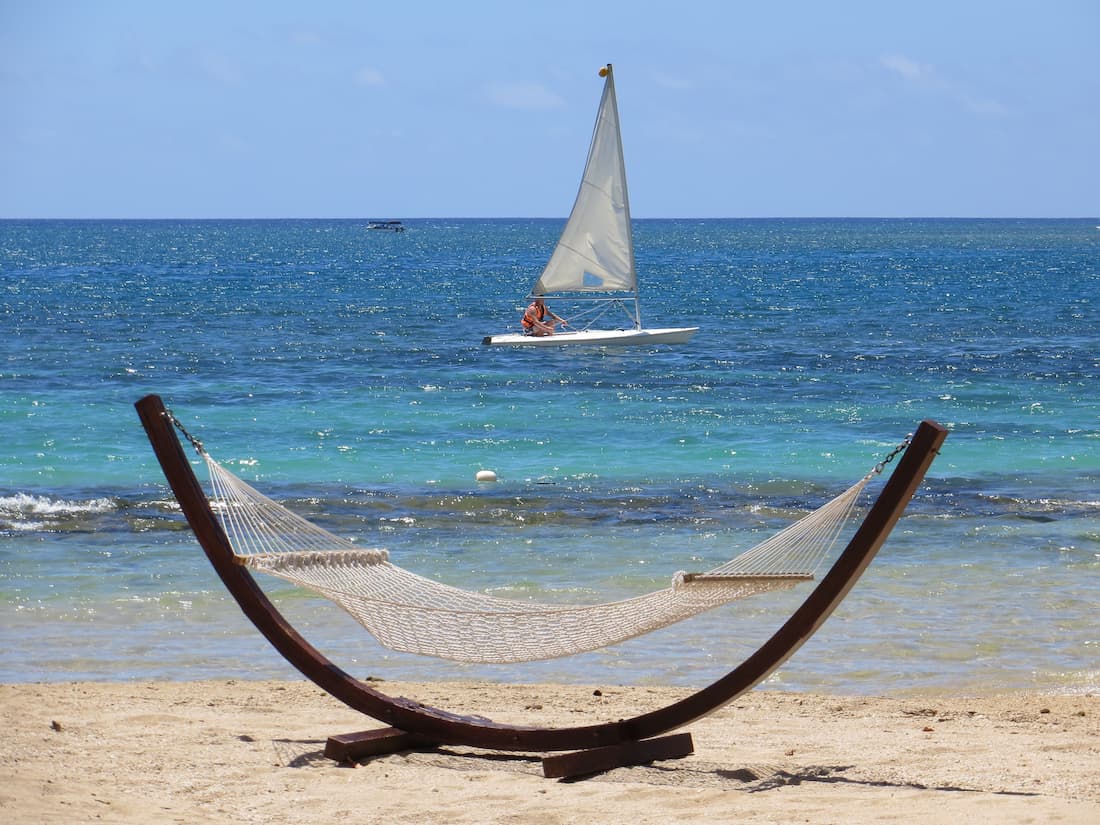 Hamaca soporte madera playa tabla surf vela chica agua turquesa Caribe Hamaca en soporte de madera en la playa y chica sobre tabla de surf con vela en agua turquesa del Caribe