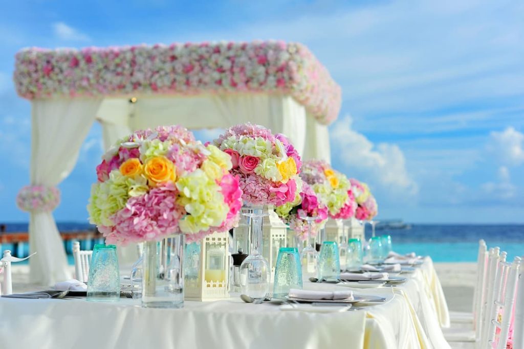 Mesa con mantel blanco, vajilla de lujo y decoración floral bajo pérgola blanca frente al mar para una luna de miel romántica