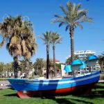 Barca de pescadores en los jardines del paseo marítimo de Salou con palmeras
