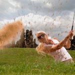 Mujer rubia elegante dando un golpe de golf en el campo verde de Sotogrande bajo el sol andaluz