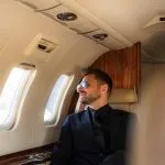 Viajero con gafas de sol mirando por la ventanilla de un avión privado rumbo a su próximo destino exclusivo