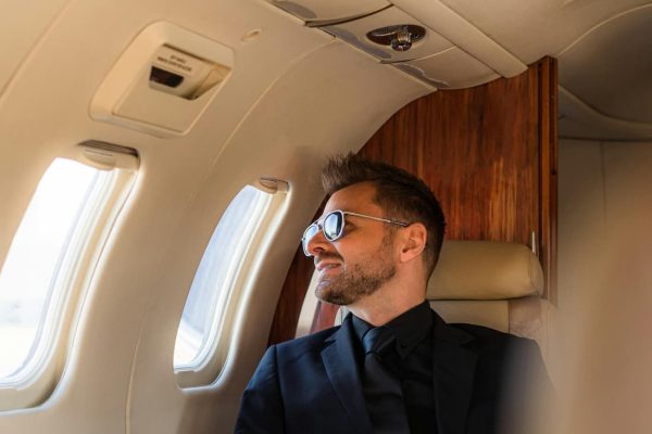 Viajero con gafas de sol mirando por la ventanilla de un avión privado rumbo a su próximo destino exclusivo