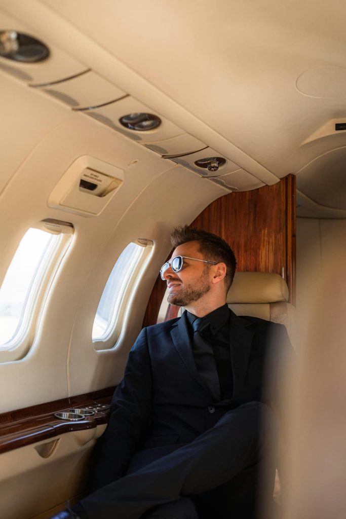 Viajero con gafas de sol mirando por la ventanilla de un avión privado rumbo a su próximo destino exclusivo