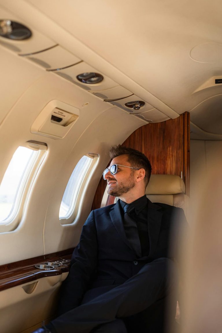 Viajero con gafas de sol mirando por la ventanilla de un avión privado rumbo a su próximo destino exclusivo
