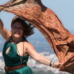 Mujer madura con vestido verde y pañuelo al viento en mirador con ciudad al fondo viajando sola después de los 50