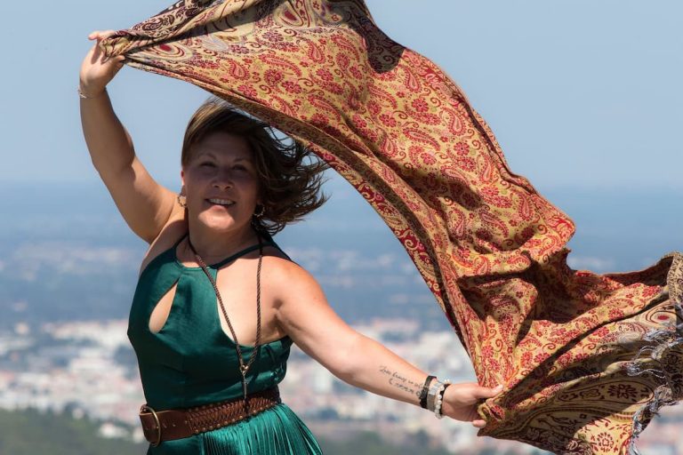 Mujer madura con vestido verde y pañuelo al viento en mirador con ciudad al fondo viajando sola después de los 50
