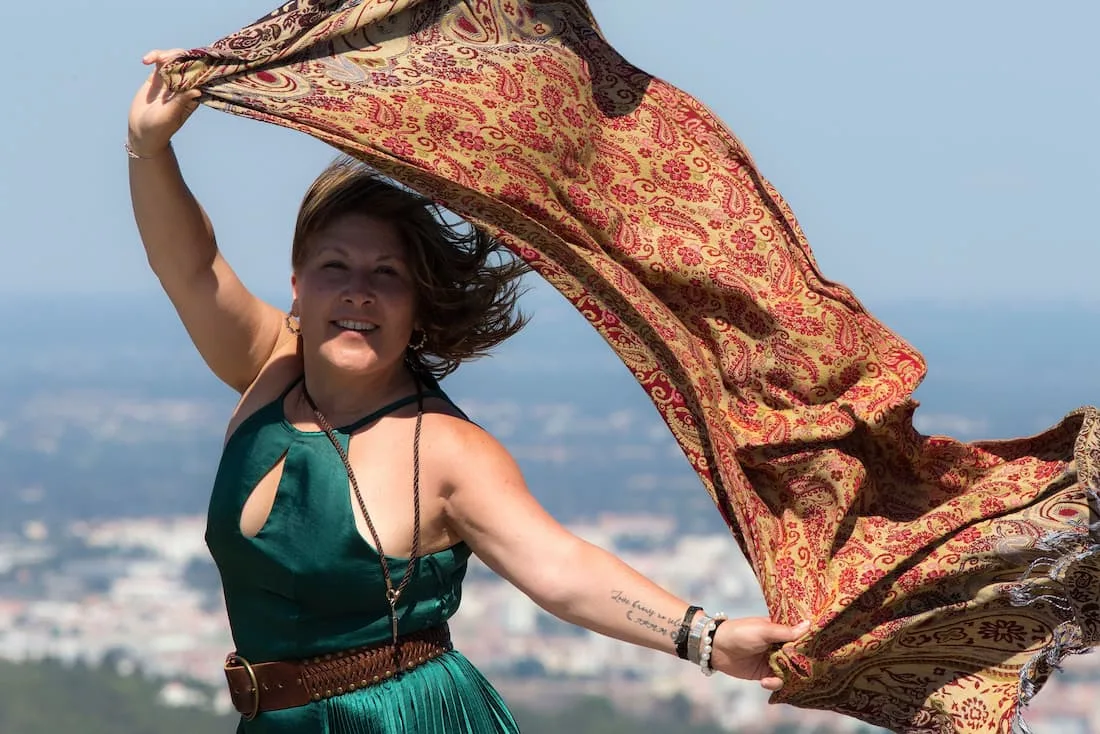 Mujer madura con vestido verde y pañuelo al viento en mirador con ciudad al fondo viajando sola después de los 50