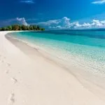 Larga playa dorada desierta con agua transparente y árboles al fondo playas de lujo en Europa